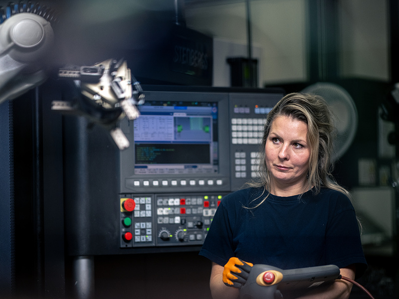 Person som står i en verkstadsmiljö och styr en robot