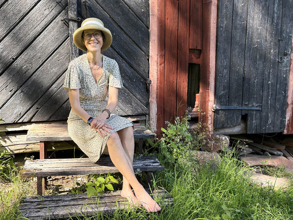 Person sitter framför en vägg och dörr utomhus i solen