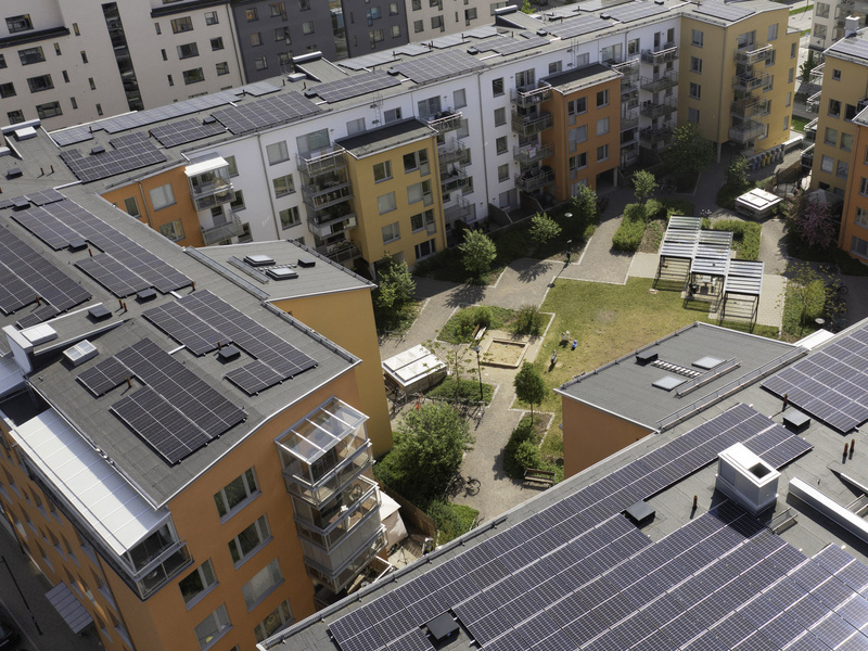 Flygfoto över flerbostadshus med solpaneler på taken runt en gemensam innergård.