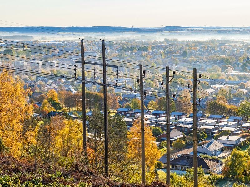 Elledningar och kraftstolpar i förgrunden framför en liten stad och berg i horisonten.