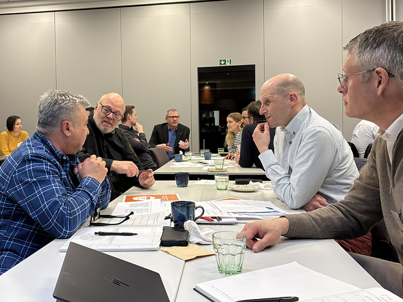 Grupper av människor sitter vid bord med många dokument på och diskuterar.