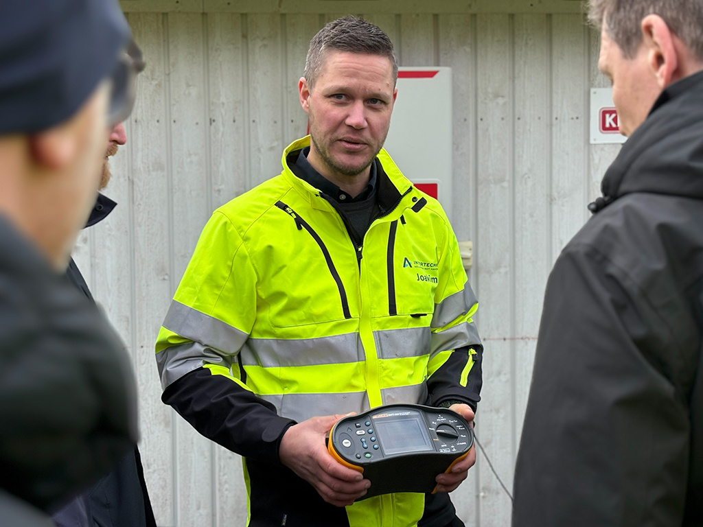 En ung man i gula varselkläder visar ett tekniskt instrument för tre andra män.