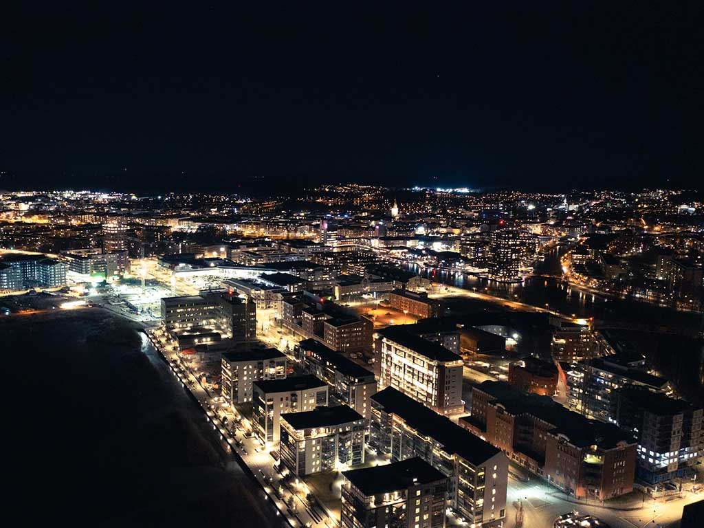 Flygfoto över Karlstad nattetid med upplysta byggnader, gator och vatten som speglar stadens ljus.