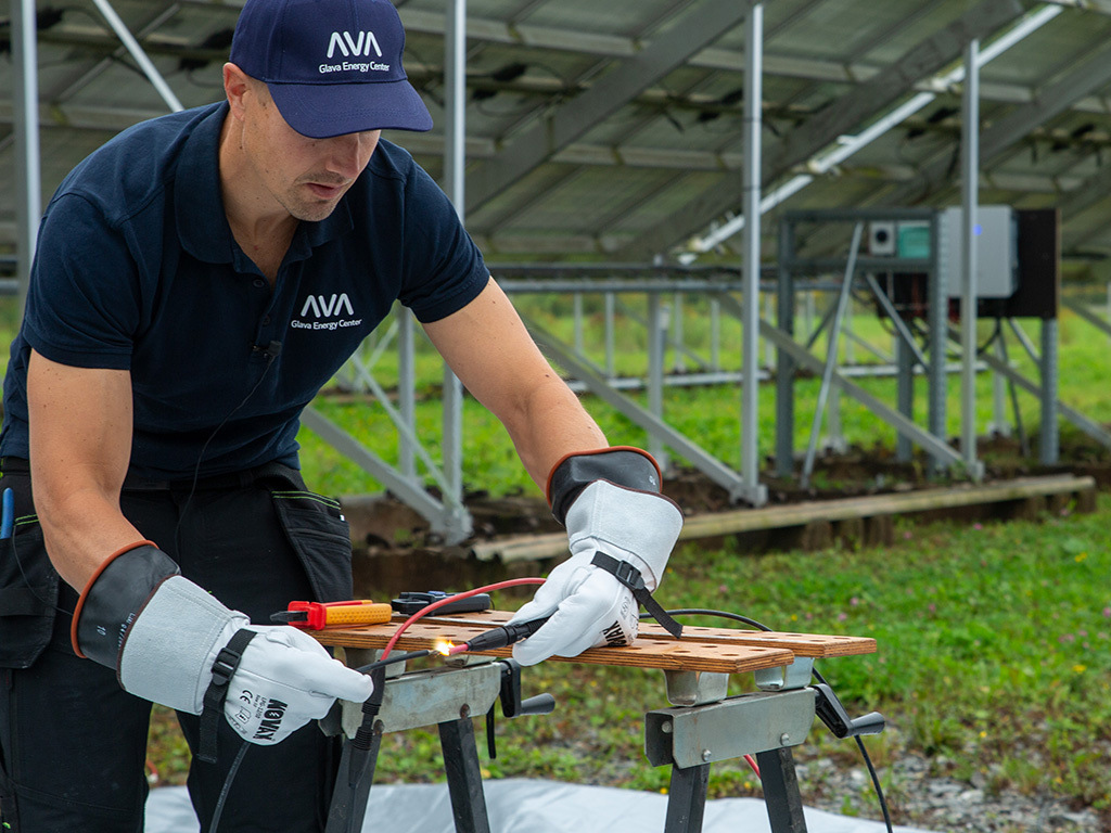 Man med arbetshandskar arbetar med elkablar i en solpanelpark.