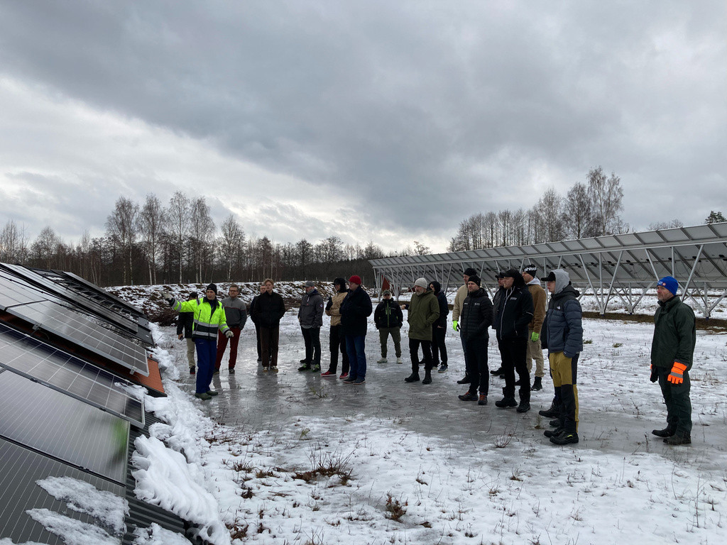 A ground of people standing in front of solar panels, in winter with show on the ground.