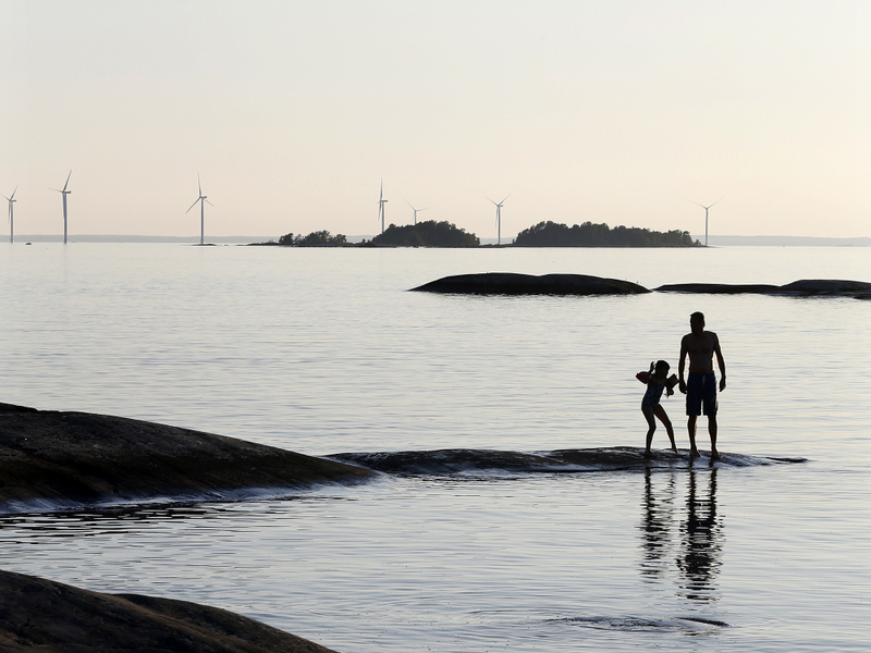 Två personer på en klipphäll vid en sjö med vindsnurror i bakgrunden.
